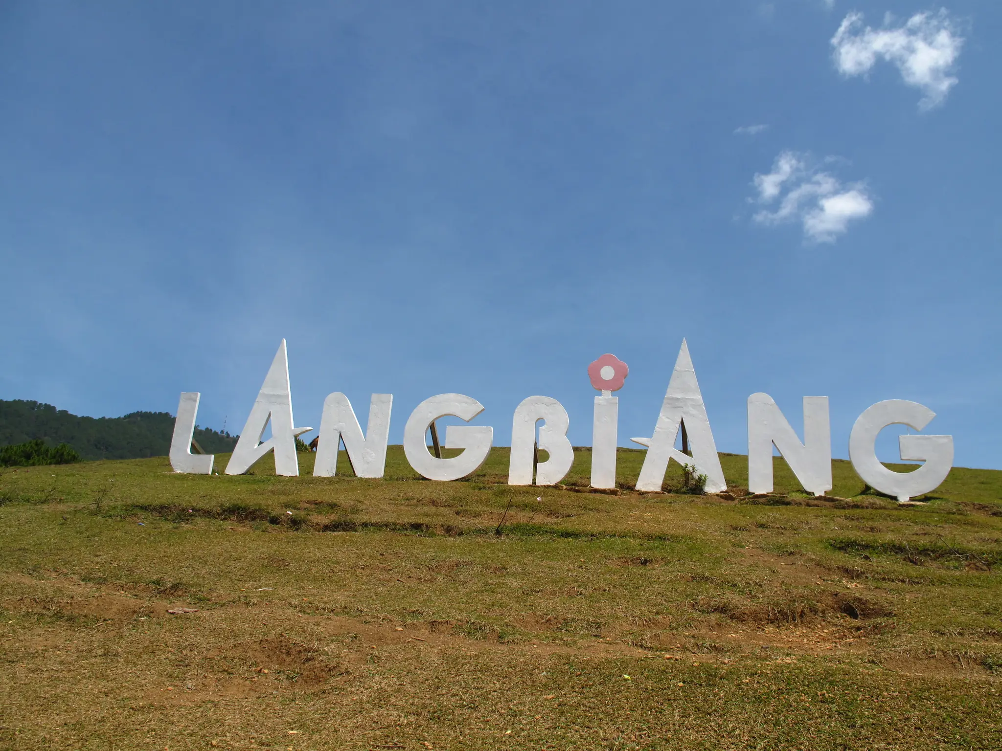 Dãy chữ LANGBIANG trắng trên đồng cỏ gần đỉnh núi, trời xanh