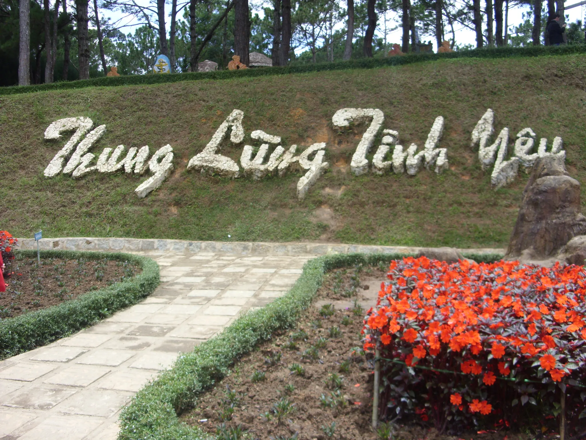 Dòng chữ Thung Lũng Tình Yêu kết bằng hoa trắng trên sườn cỏ, bên lối đi và bồn hoa đỏ