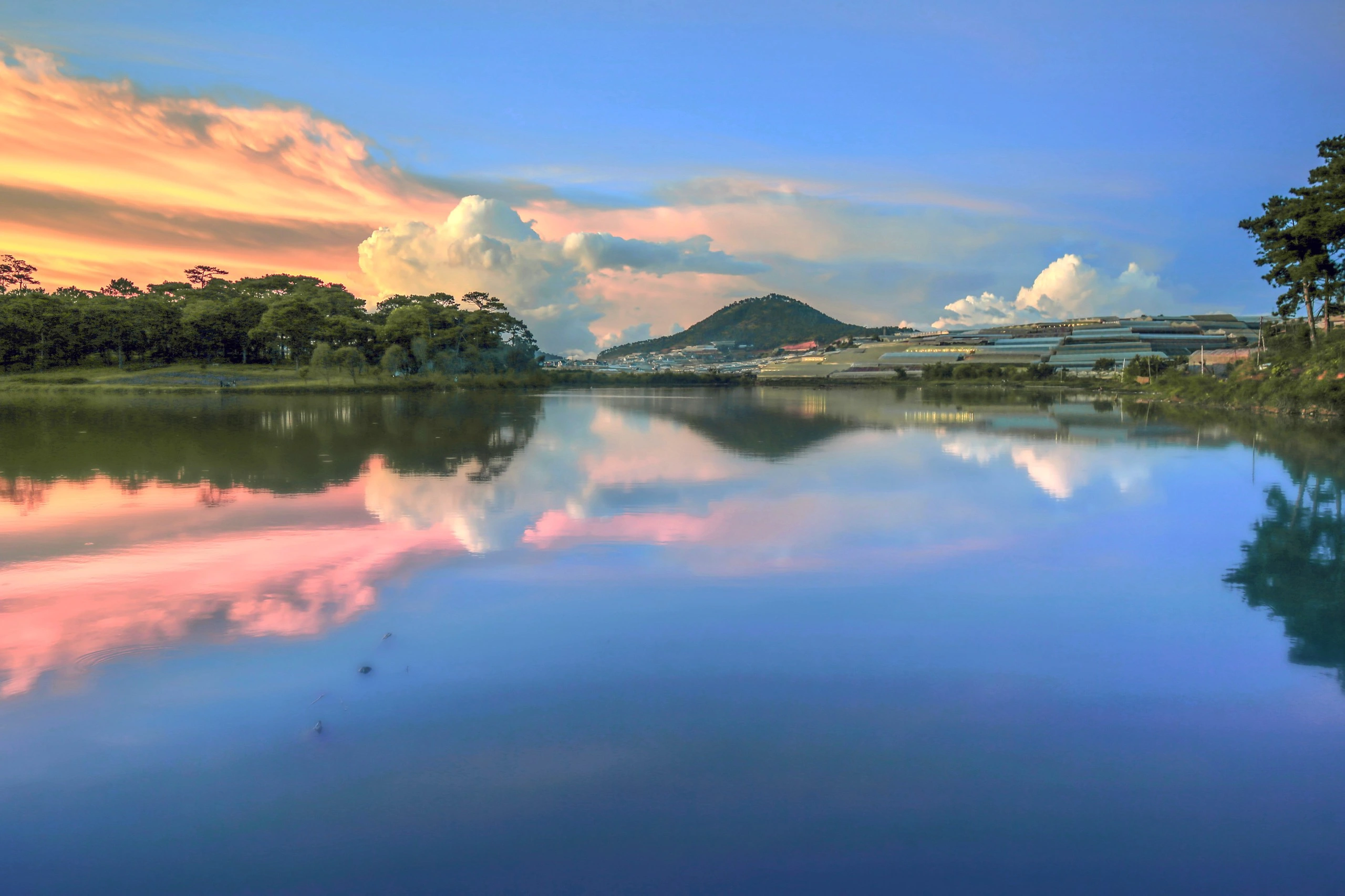 Mặt hồ Than Thở phẳng lặng in bóng mây hồng lúc hoàng hôn, xa xa là đồi thông và vùng nhà kính
