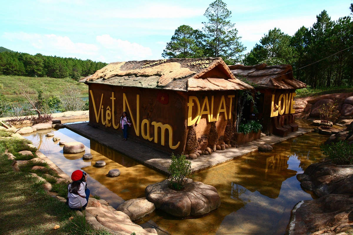 Ngôi nhà đất đỏ bazan không nung đắp chữ "Việt Nam - Đà Lạt" màu vàng, bao quanh là hồ nước nông